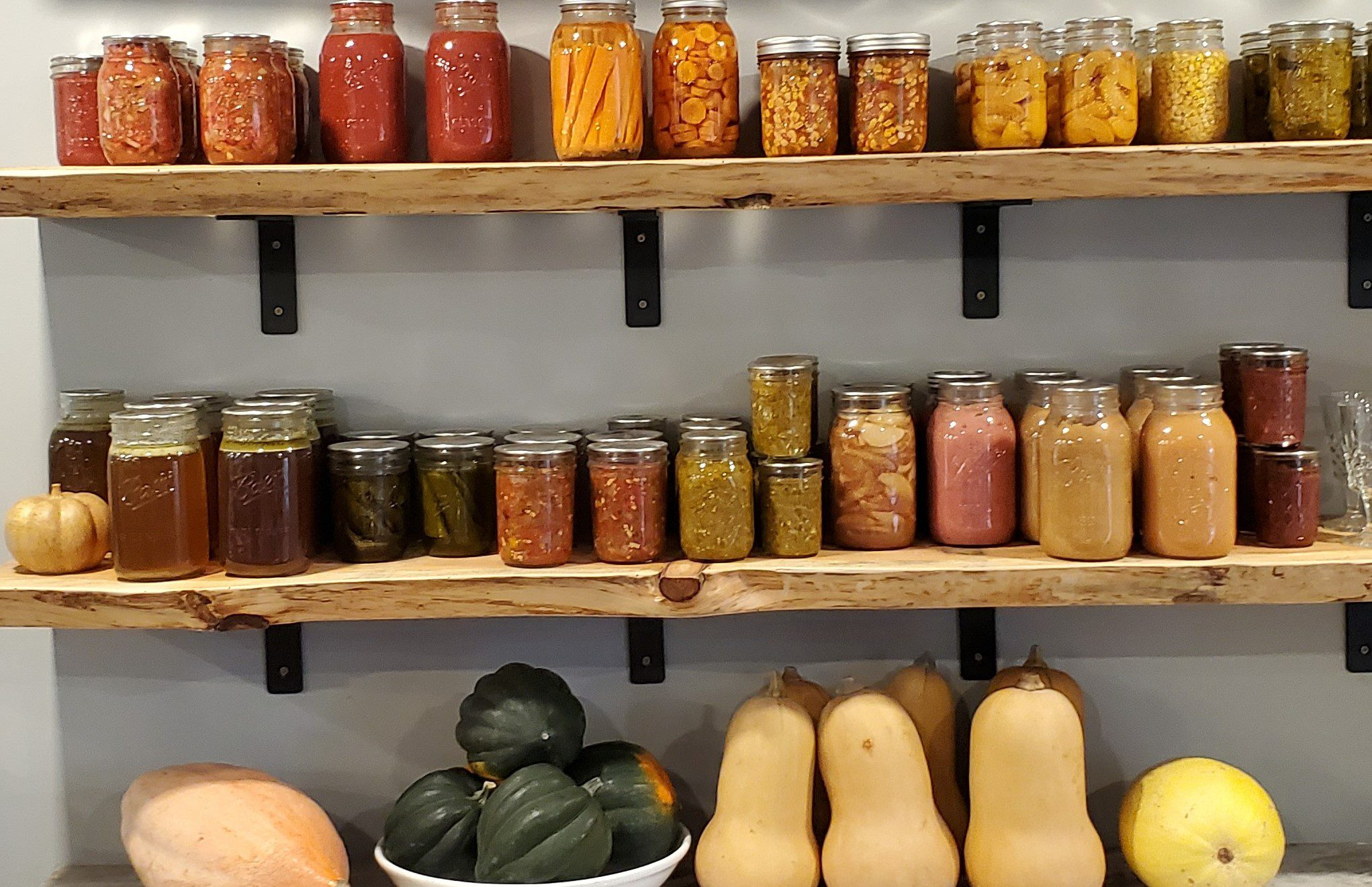 A picture of jars of Peaches. Pickles. Applesauce on a shelf